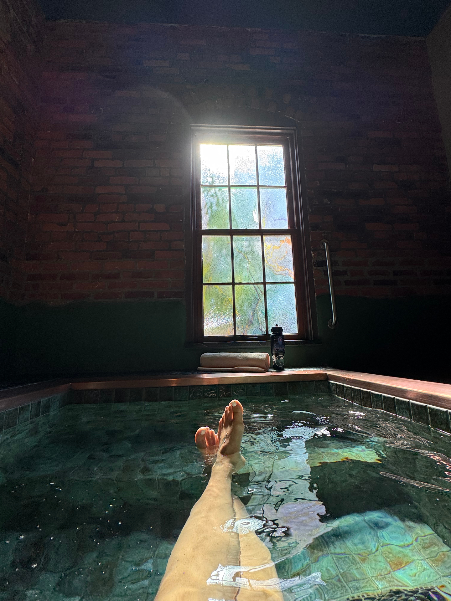 Soaking in a brick-walled hot spring with sunlight pouring through a window